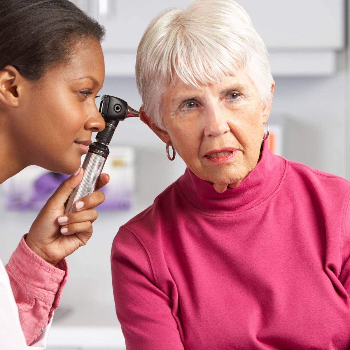 Doctor examines elderly woman's ear with an otoscope.