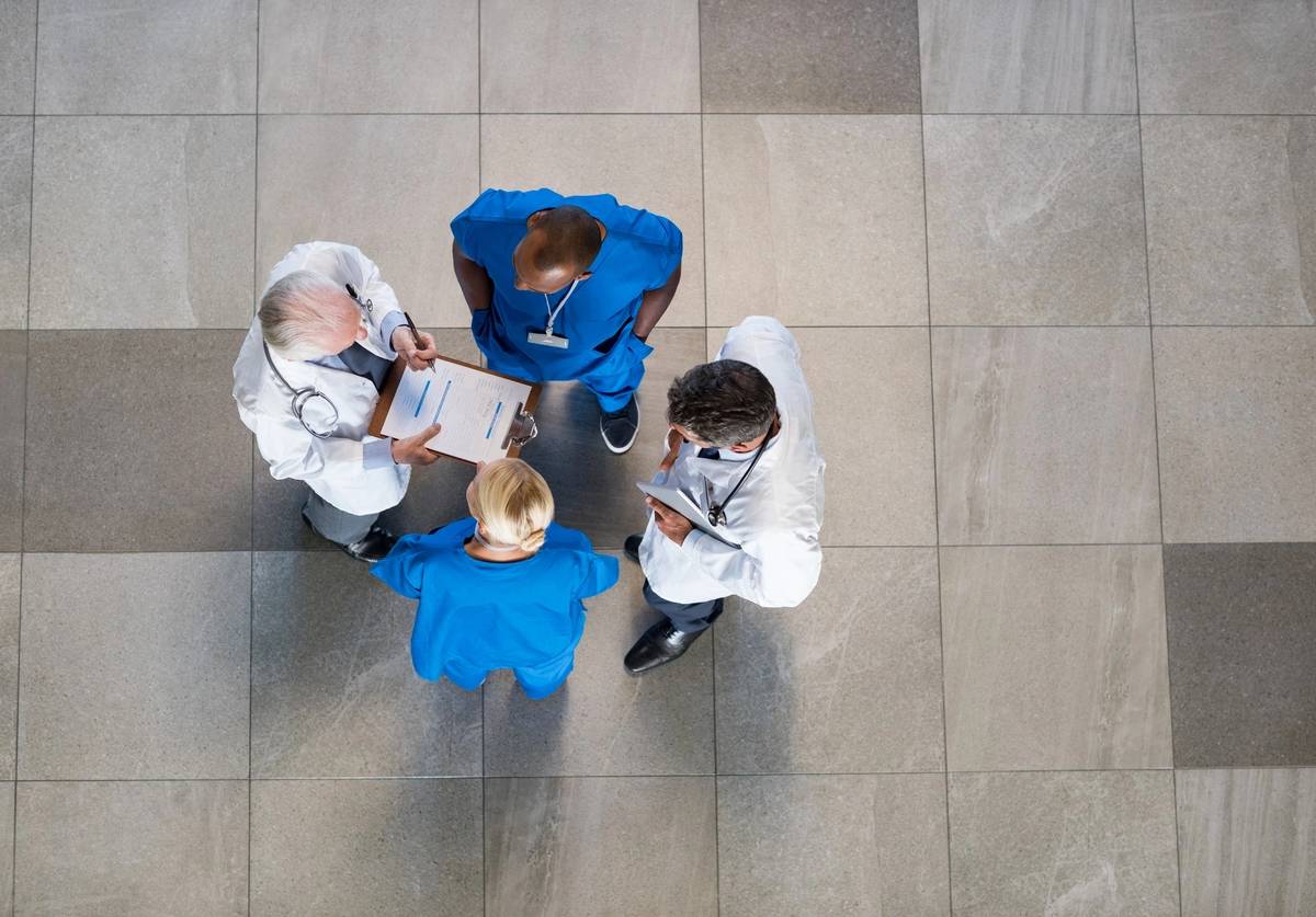 A group of medical professionals discussing over a clipboard in a hospital corridor.