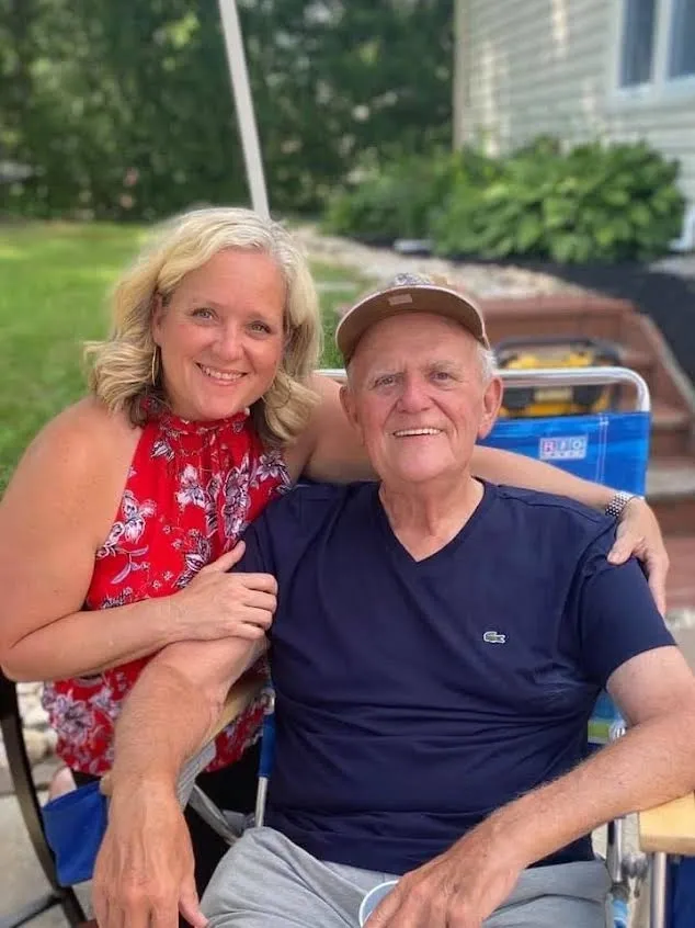 Woman hugging elderly man outdoors, both smiling