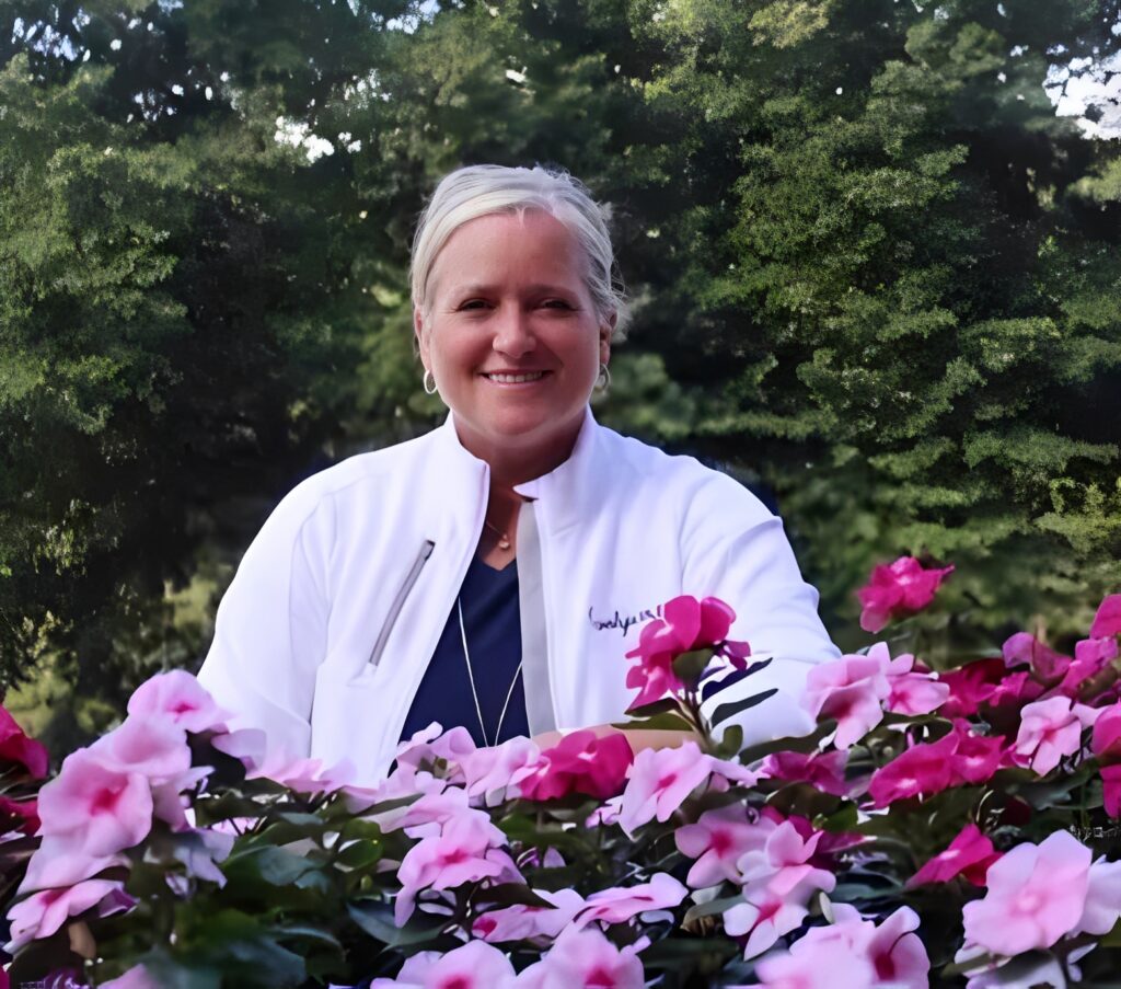 Smiling woman in white jacket behind flowers
