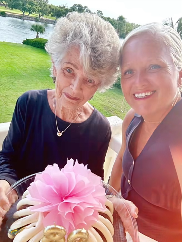 Smiling women celebrating with a decorated cake.